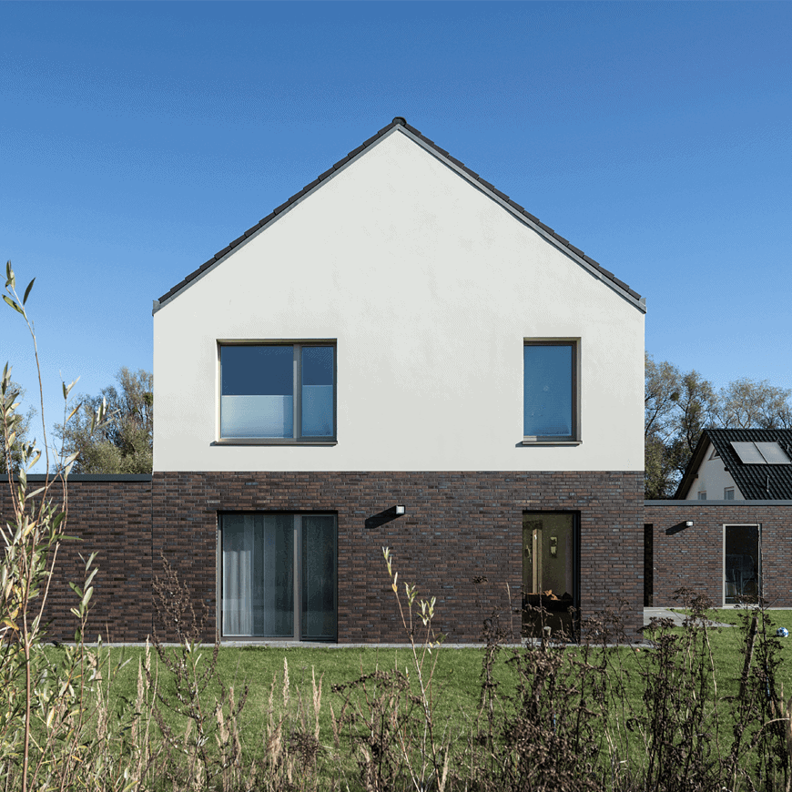 Modernes Einfamilienhaus mit Satteldach, heller Putzfassade und Sockel aus dunkelbraunen Klinkern