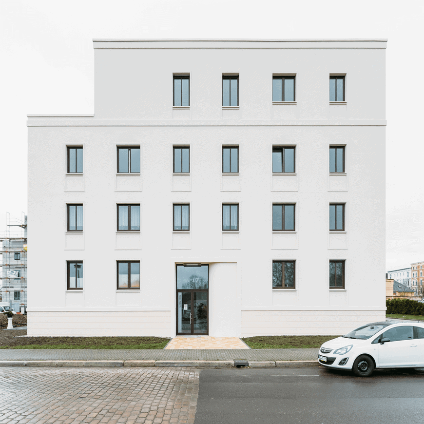 Frontalansicht eines modernen Mehrfamilienhauses mit weißer Putzfassade und Sockel